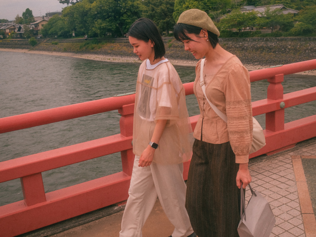 Two women walking across a red bridge beside a river