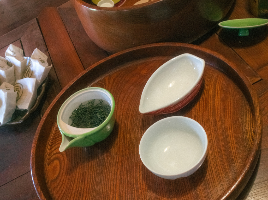 Traditional tea set with loose green tea leaves in a small ceramic pot and empty cups on a wooden tray