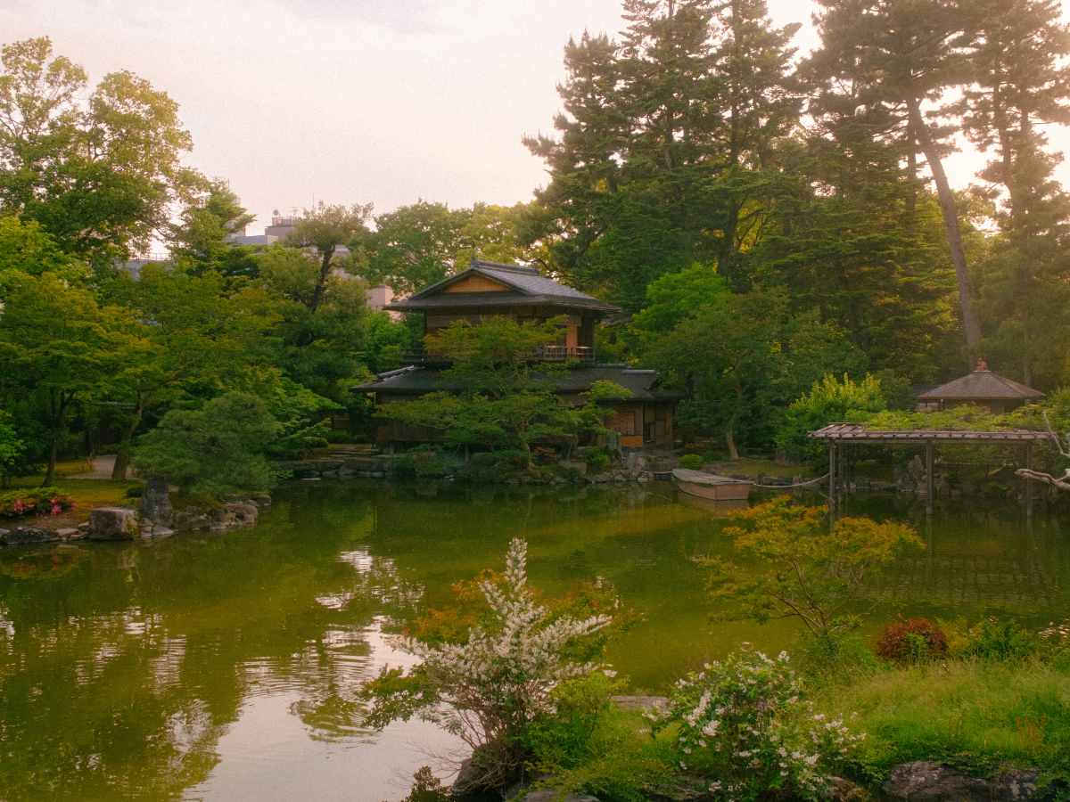 Traditional Japanese garden with a wooden teahouse beside a calm pond surrounded by trees