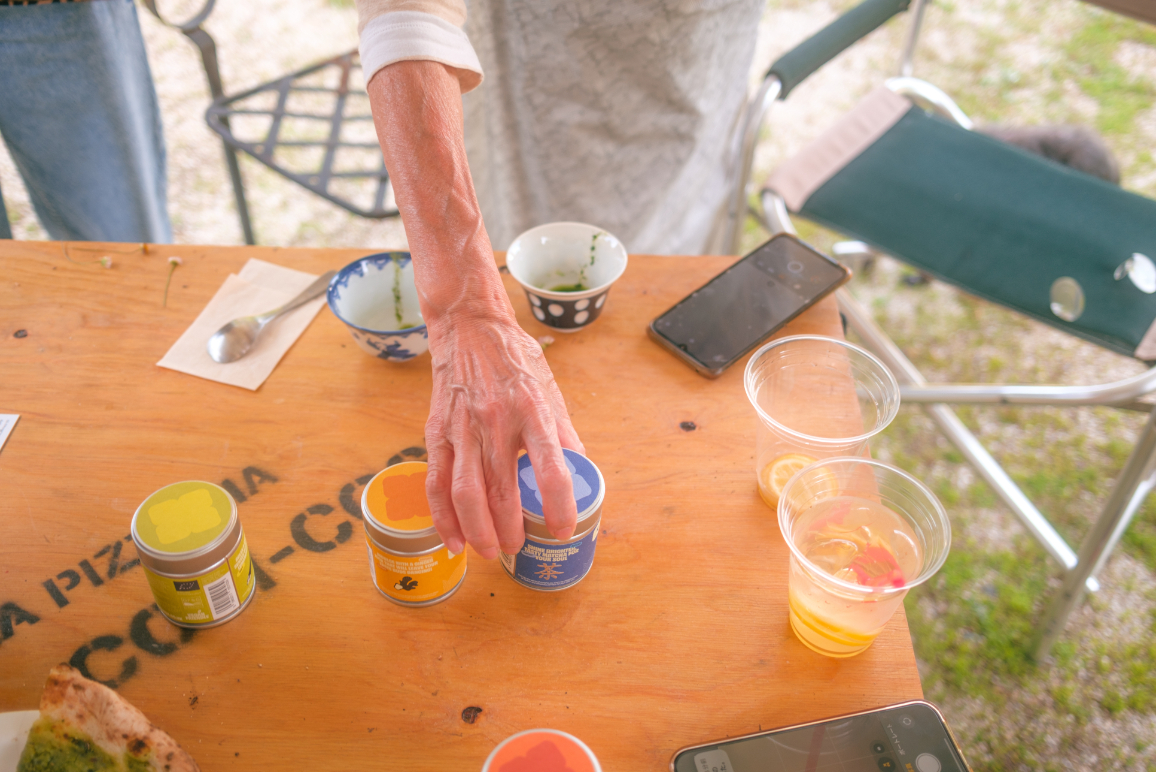 Hand reaching for OSSU matcha tins on a wooden table outdoors