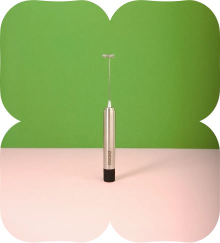 Handheld electric matcha whisk standing upright on a green and pink background