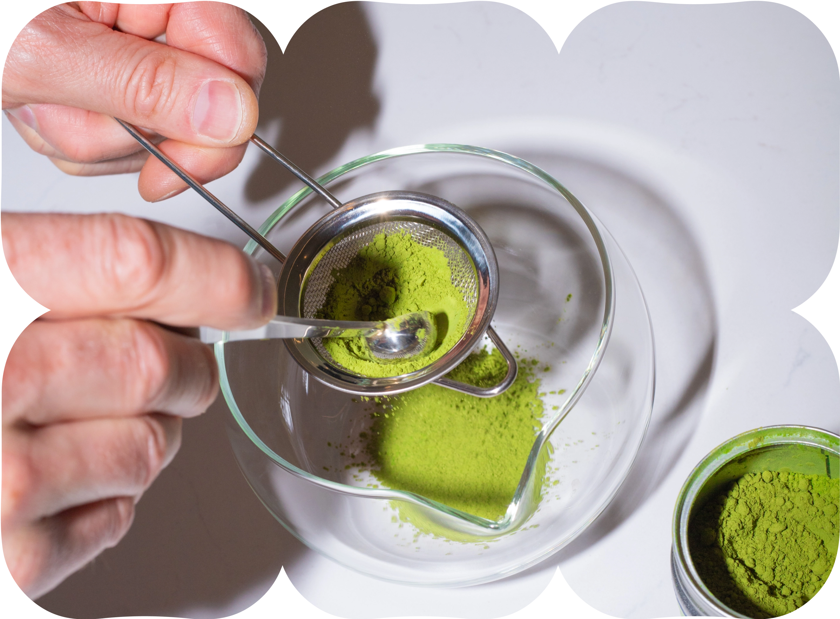 Hand sifting bright green matcha powder through a metal sieve into a glass bowl.