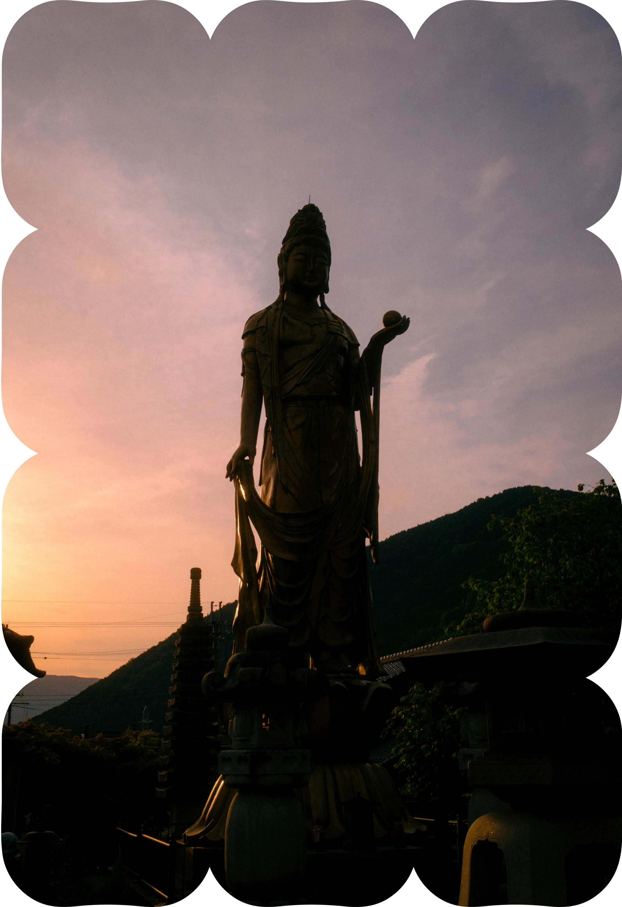 Silhouette of a large Buddha statue at sunset with mountains in the background