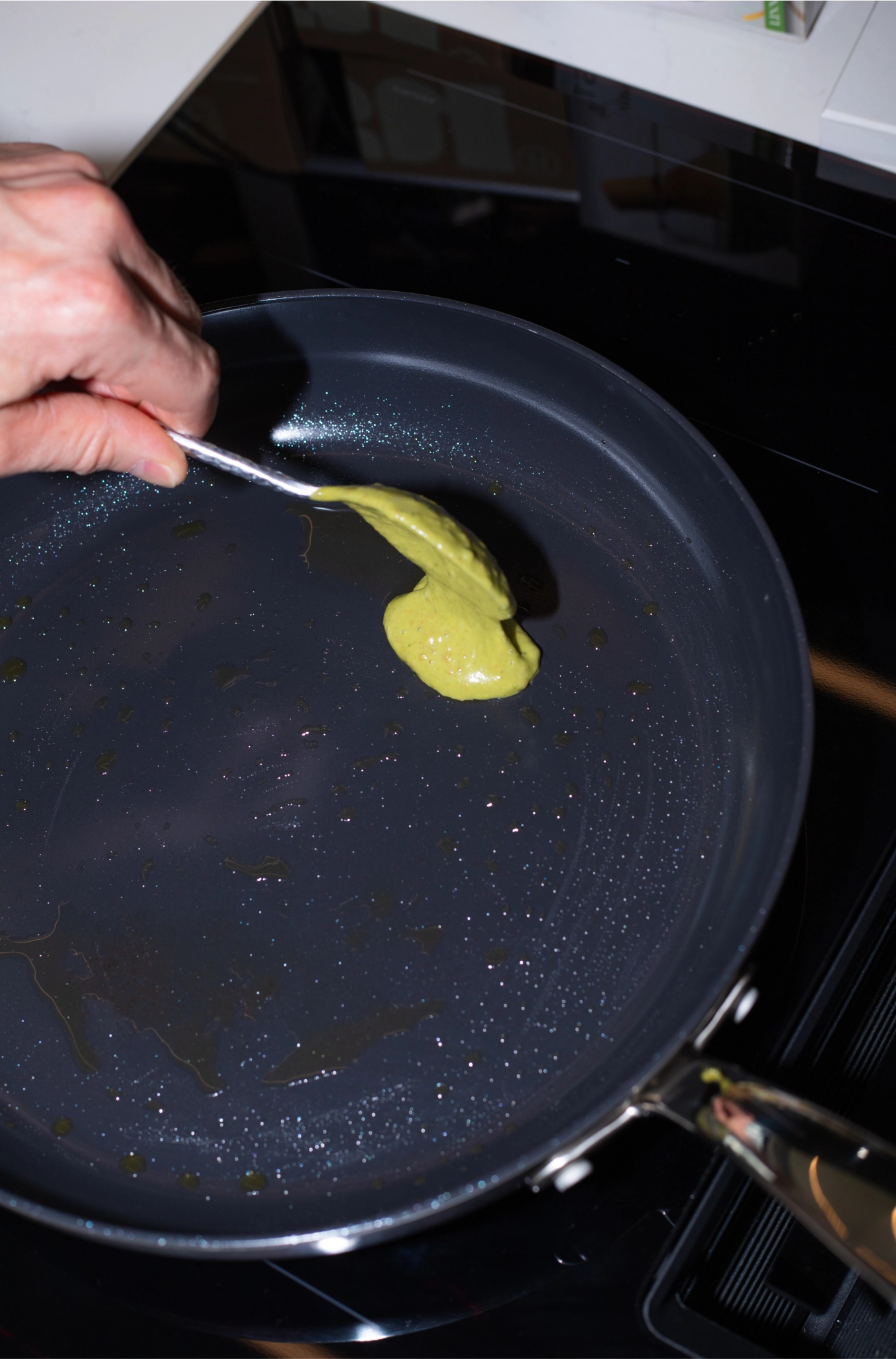 A spoon dropping green matcha batter into a heated frying pan on a stovetop
