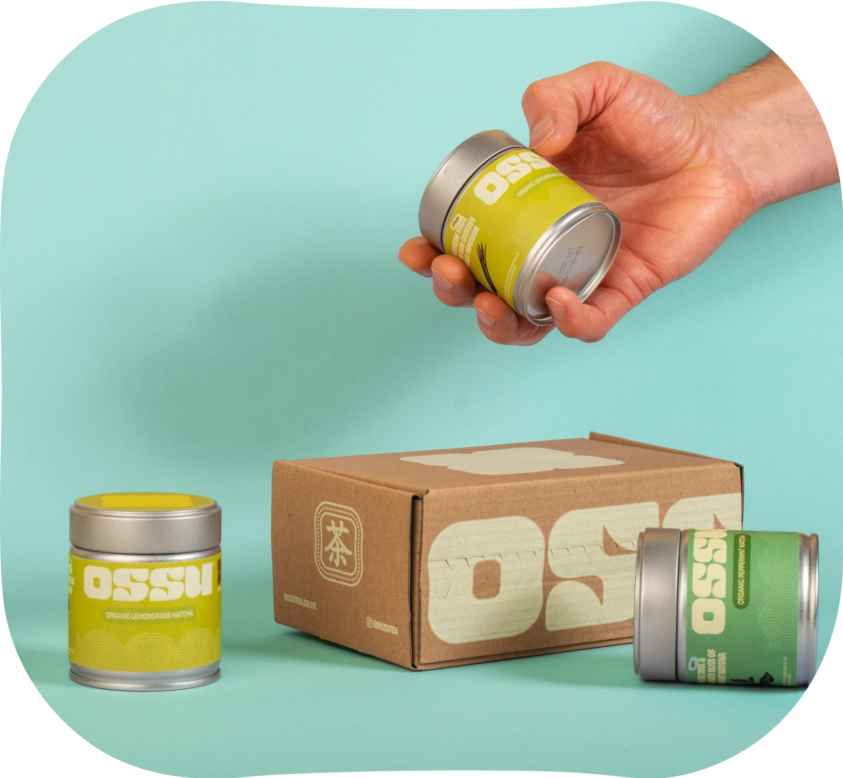 Hand holding OSSU matcha tin above branded box with flavoured matcha tins beside it