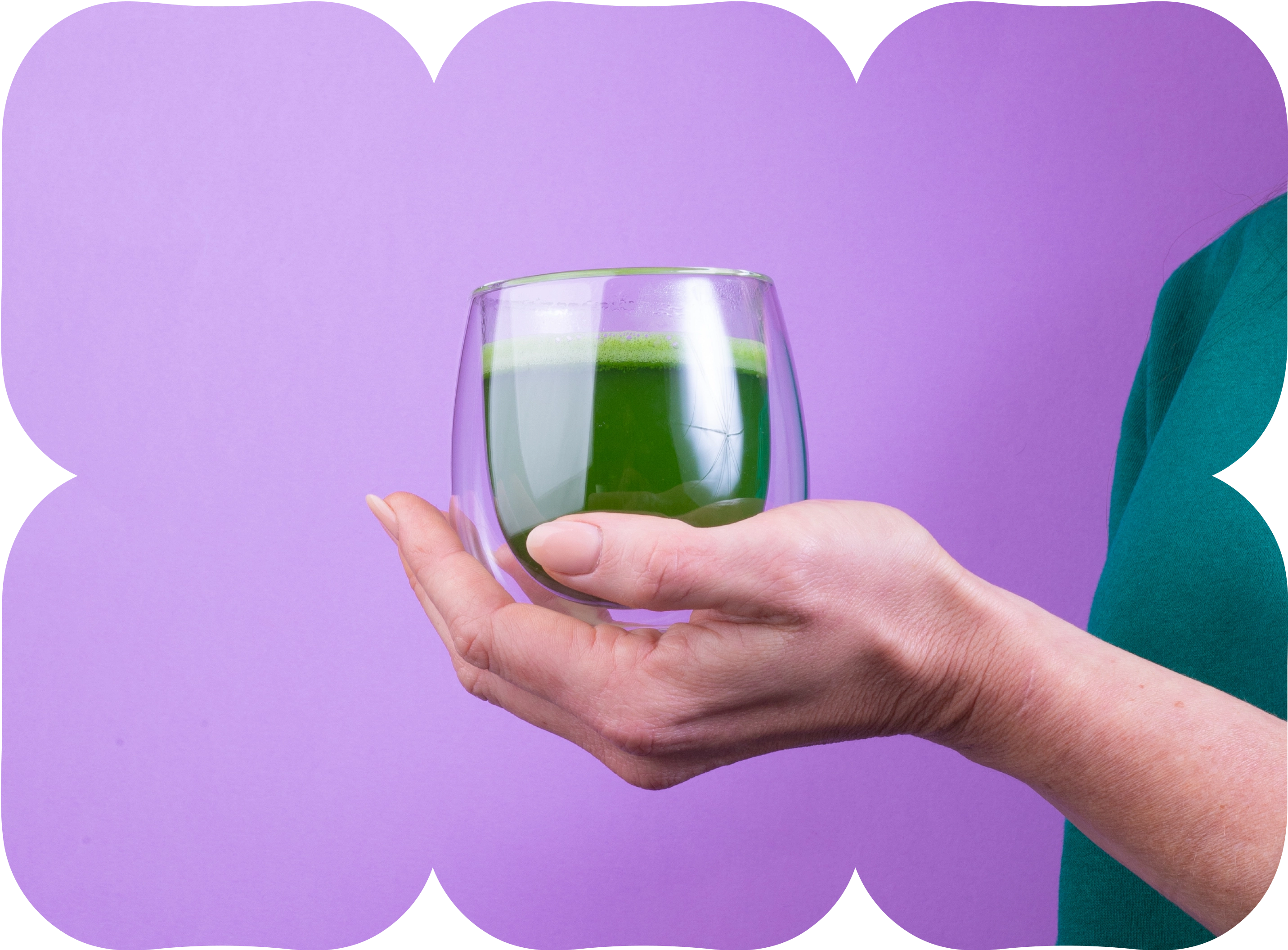 Hand holding a clear glass cup of green matcha drink against a purple background