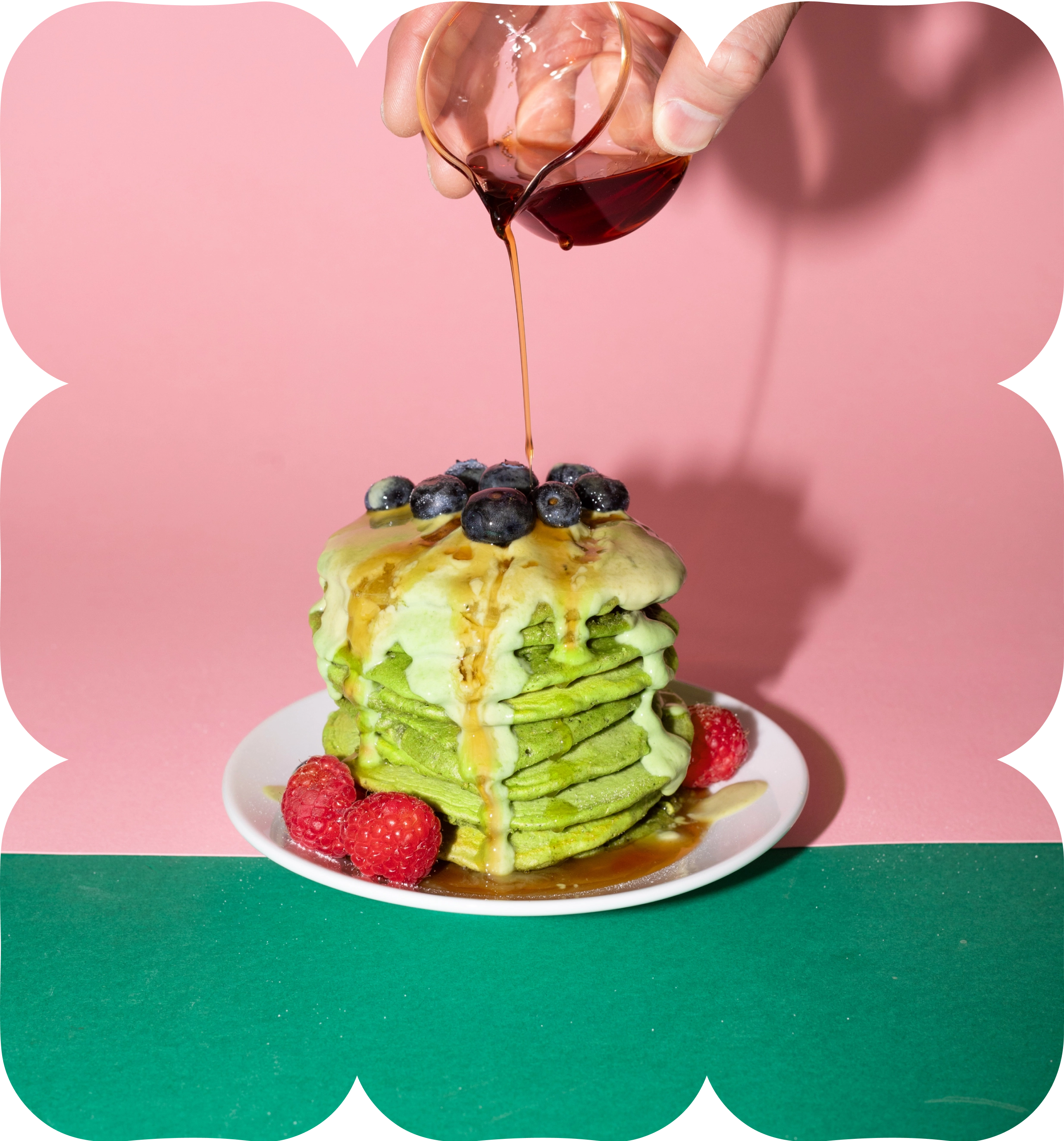Stack of green matcha pancakes topped with blueberries and raspberries as syrup is poured over