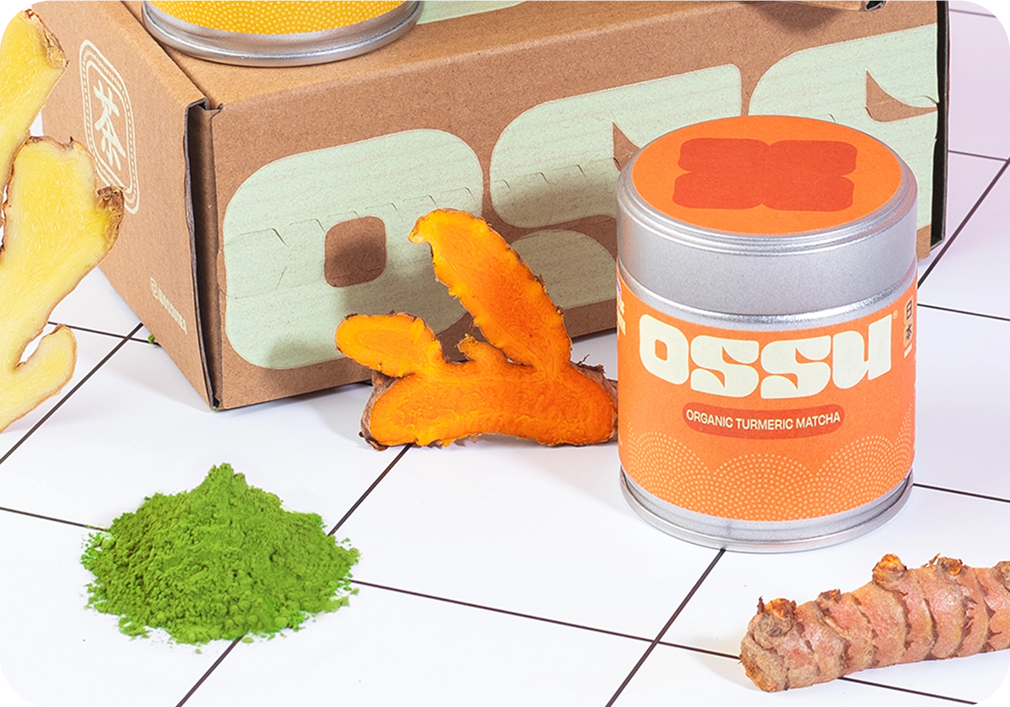 OSSU organic turmeric matcha tin with fresh turmeric root and loose matcha powder beside OSSU branded box