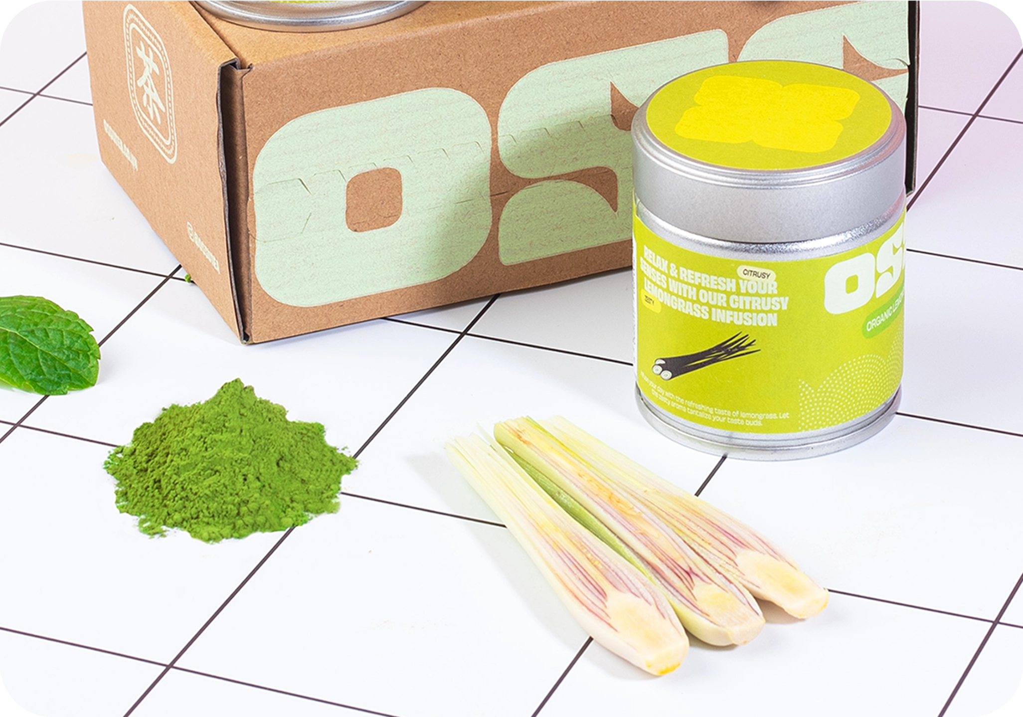 OSSU organic lemongrass matcha tin with fresh lemongrass stalks and loose matcha powder beside OSSU branded box
