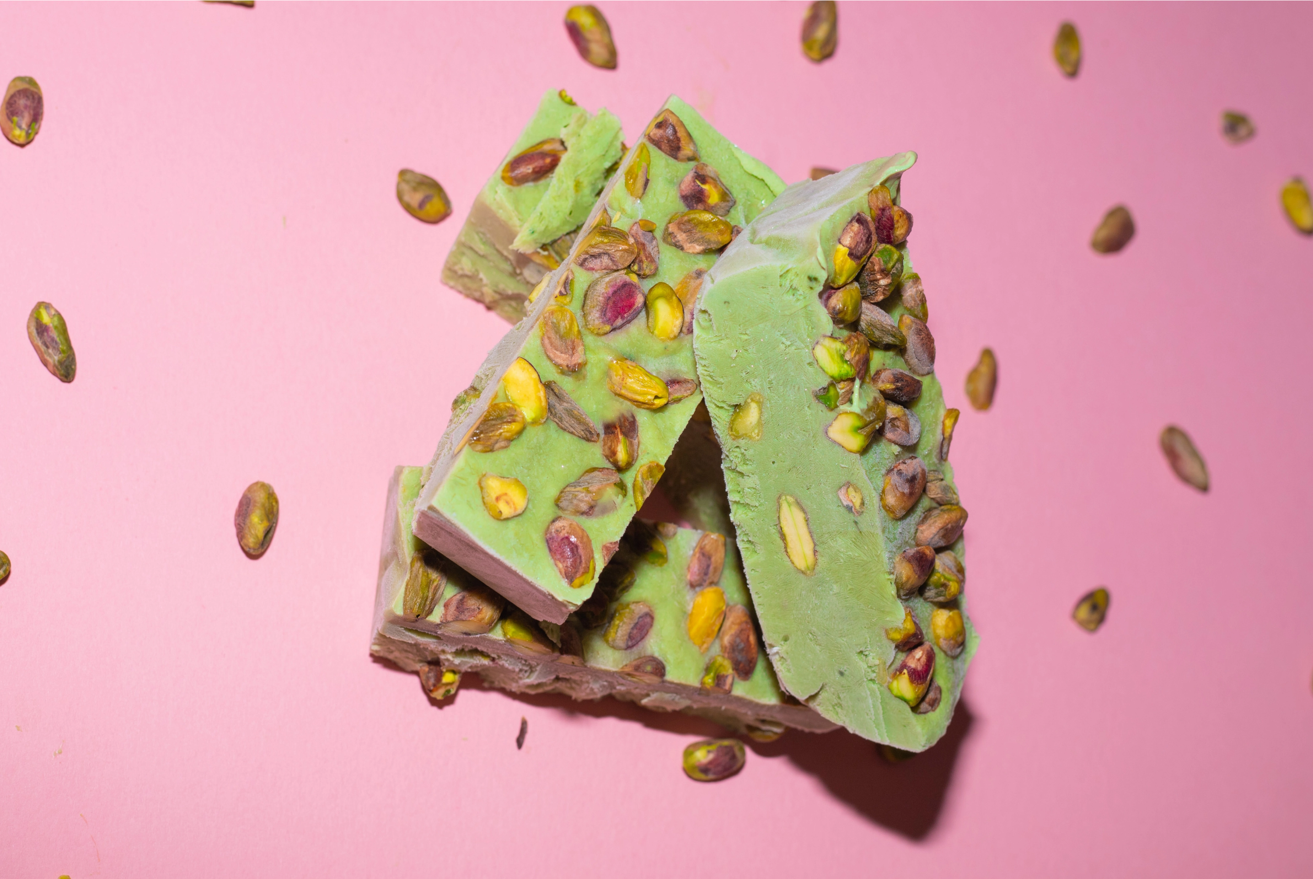 Matcha frozen yoghurt mixture in a parchment-lined tray topped with chopped pistachios