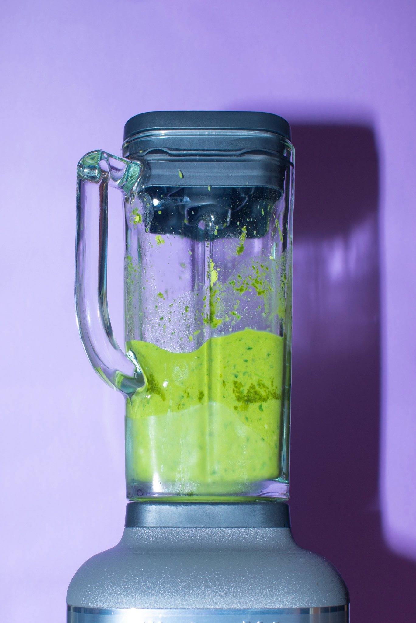 Glass blender jar blending a bright green matcha smoothie against a purple background