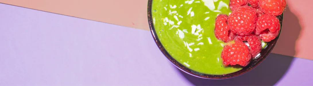 Close-up of a smoothie bowl of bright green matcha topped with fresh raspberries and coconut flakes